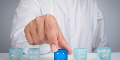 Customer service evaluation, feedback, rating, client experience Customer service evaluation, feedback, rating, client experience, and satisfaction survey concepts. The businessman's hand chooses the happy smile face icon on blue cube on table and white background.